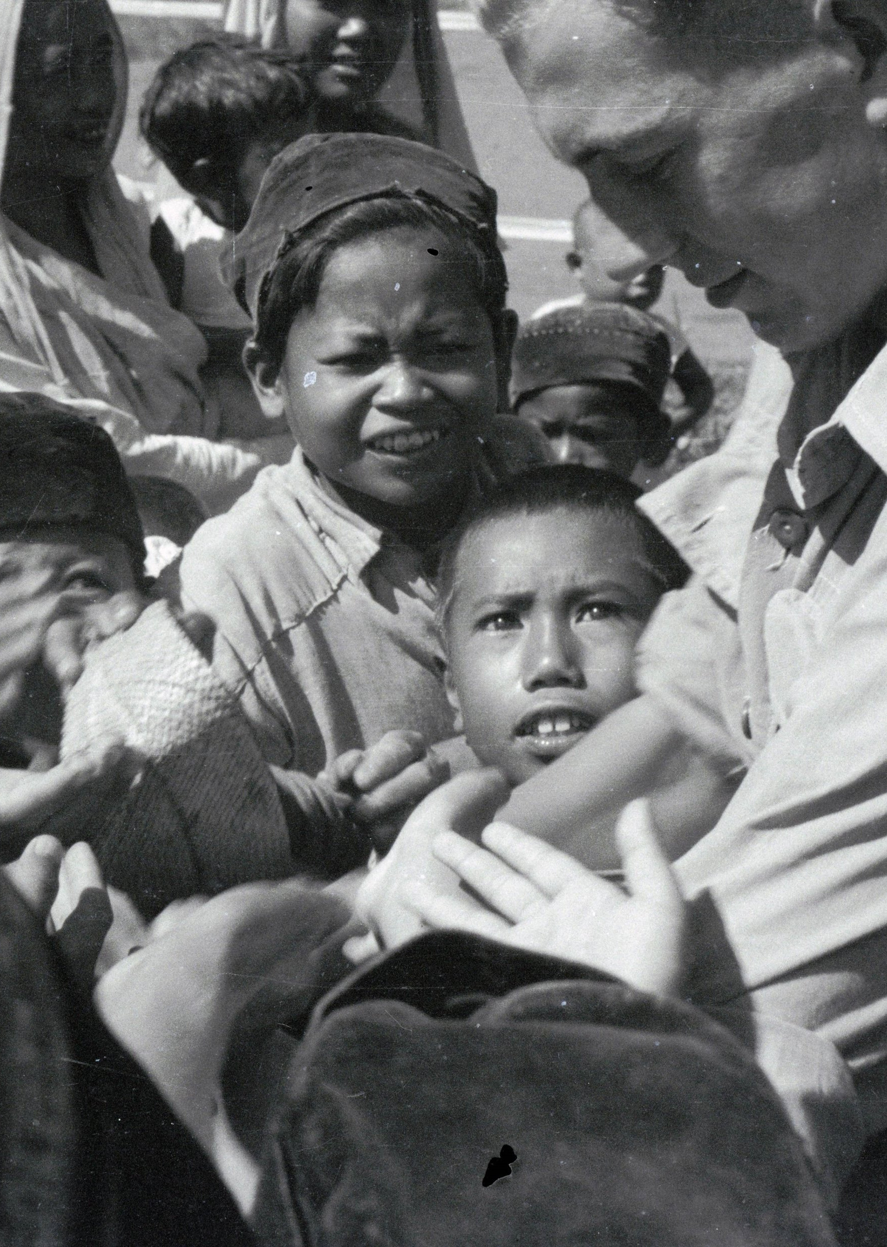 Uitdelende Nederlandse militair omringd door kinderhanden tijdens de feestelijkheden in Cipanas (Java) © Erven C.J. Taillie
