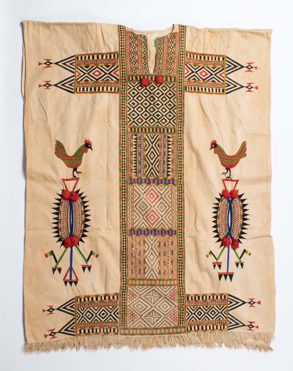 . Beige boubou uit Djenné (1971-2006), versierd met machinaal borduurwerk, franjes en pompons. De meeste borduursels zijn abstract (strepen, driehoeken en ruiten), met twee rode en groene hanen aan de zijkanten. De zak is aan beide kanten toegankelijk. (7269-3)