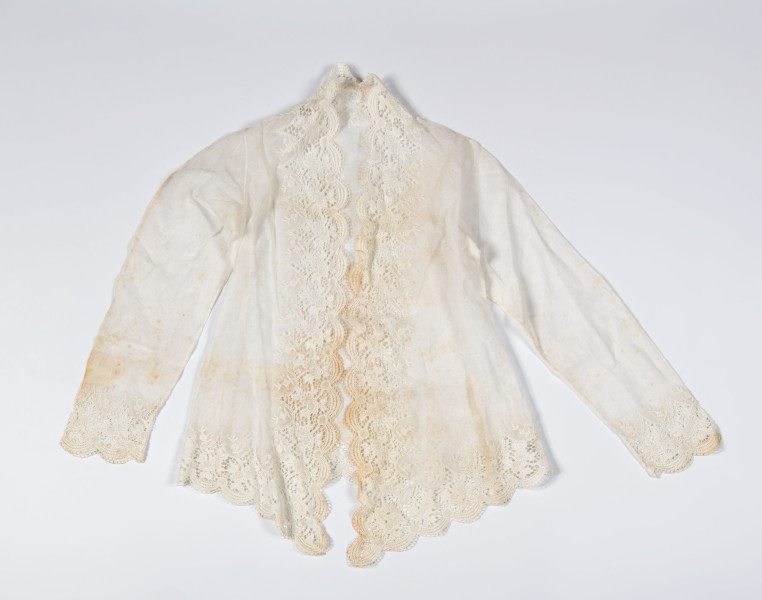 Deze witte kebaya is een typisch voorbeeld van de Kebaya Encim die gangbaar was vanaf 1930. De zeer dunne, transparante stof heeft een ingeweven motief. De (machinale) gelobde kantrand is er heel nauwkeurig ingezet en kleine geborduurde bloemen op steel zijn er aan toegevoegd. (7292-5) 