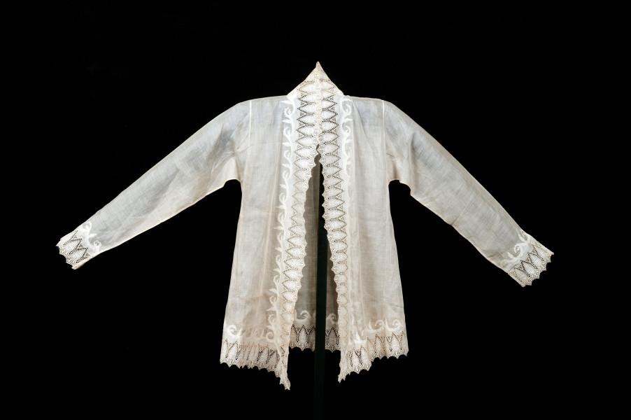 Ook deze kebaya was ooit wit, maar is sterk vergeeld. De randen zijn dubbel gedecoreerd. Aan de buitenrand is kant vastgezet. Daarnaast is een extra sierborder gemaakt door een extra stuk stof erop te stikken en weg te knippen langs de stikselrand. Een bewerkelijke techniek, die wijst op een maakster die hier ervaring in had, wat volgens de overlevering klopt met vermoedelijke draagster Han Tek Nio. (RV-6225-1)