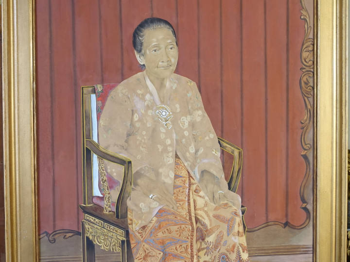 Op dit geschilderde portret van Jo Heng Nio (1827-1900) draagt zij een kebaya samen met een gebatikte kain en geborduurde muiltjes. Jo Heng Nio was de derde vrouw van stamvader Kan Keng Tiong, en de betovergrootmoeder van Sioe Yao Kan en Gie Tjin Kan. (7095-3)