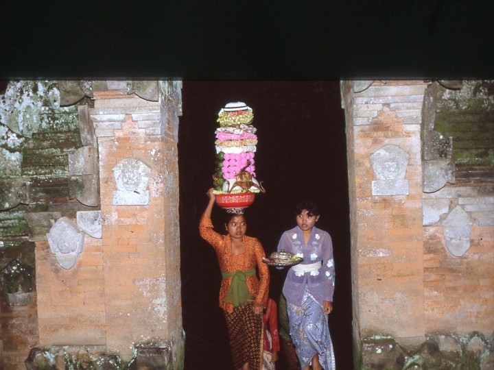 Vrouwen in gekleurde kebaya’s komen de Pura Dalem in Ubud binnen met hun offers. De Pura Dalem is een Dodentempel, een van de drie hoofdtempels in een dorp, 24 mei 1983. Vroeger droegen vrouwen bijna altijd een kebaya in één van de kleuren van de regenboog. (7358-75) ©Francine Brinkgreve.